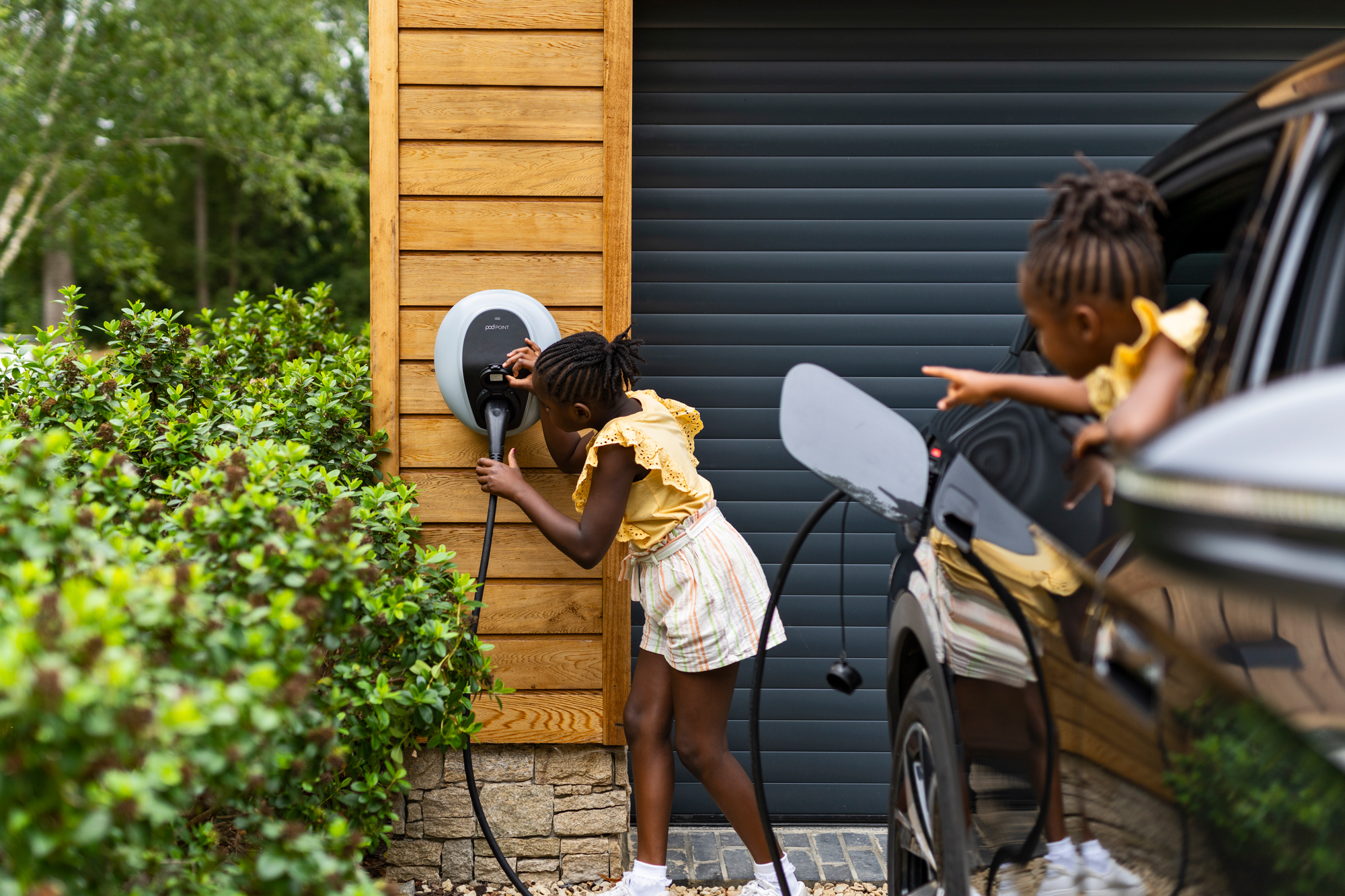 A close up of two sisters plugging their family EV into a Pod Point Solo 3