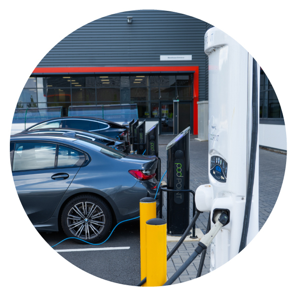 A dark grey car plugged into a Pod Point twin charger, with an unused Pod Point Velocity charger in the space next to it