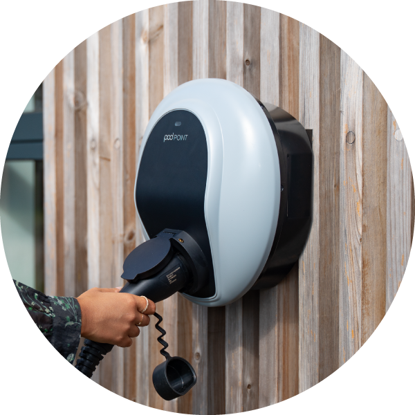 A women's hand is plugging a cable into a Pod Point Solo 3 installed on a wooden slat wall