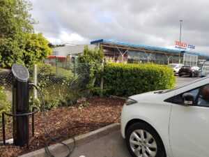 A white EV plugged in to a Pod Point twin charger at a Tesco Extra car park