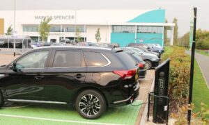 A side shot of a black SUV parked in a green EV charging bay and plugged into a Pod Point twin charger