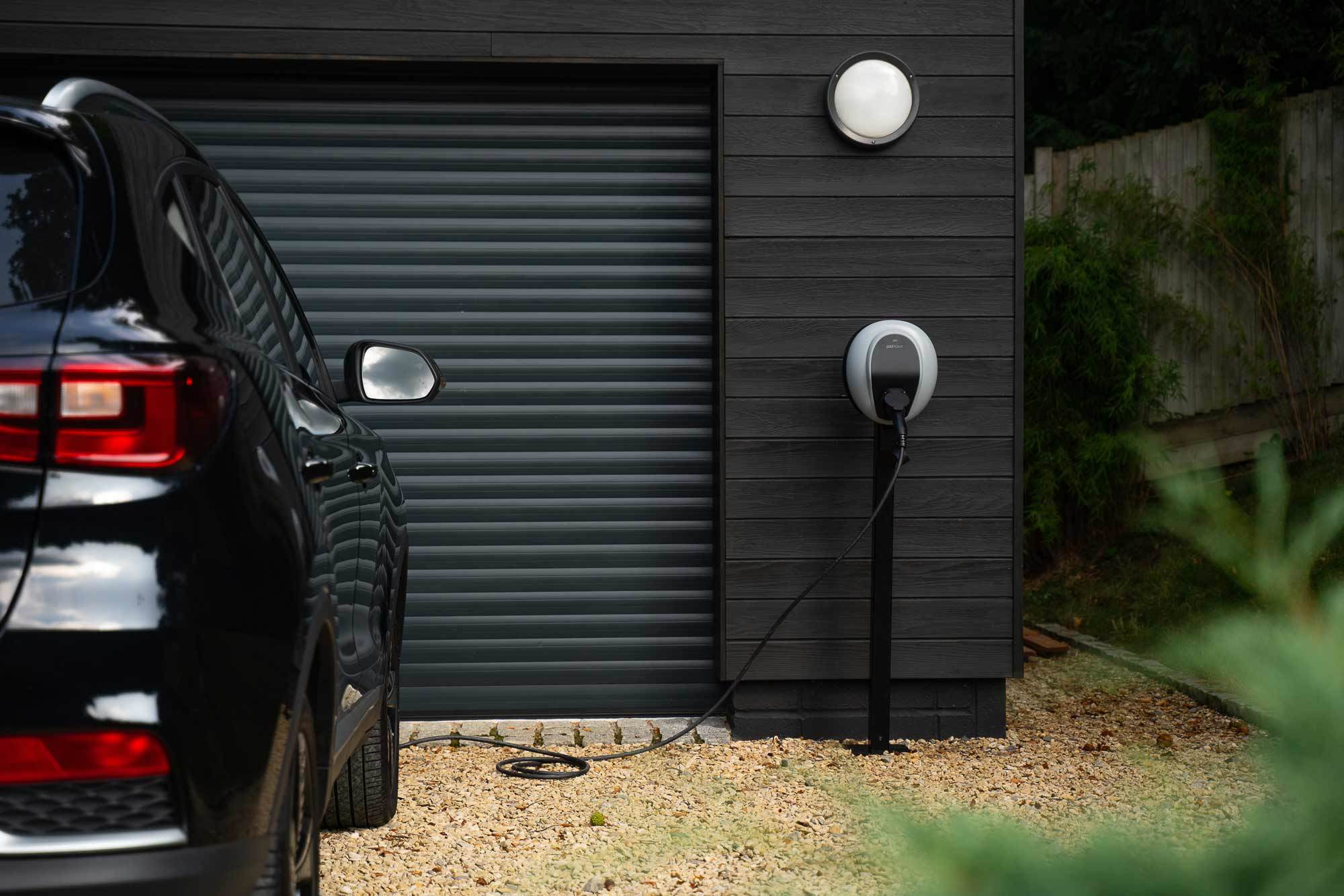 A wide shot of a Solo 3 installed on a black wooden wall of a garage, with a black EV parked on the left and plugged in to the charger