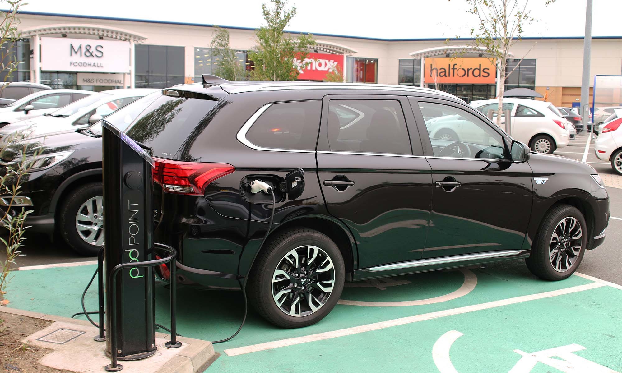 A diagonal shot of a black SUV reversed into a green EV charging bay at Savills car park, plugged into a Pod Point twin charger