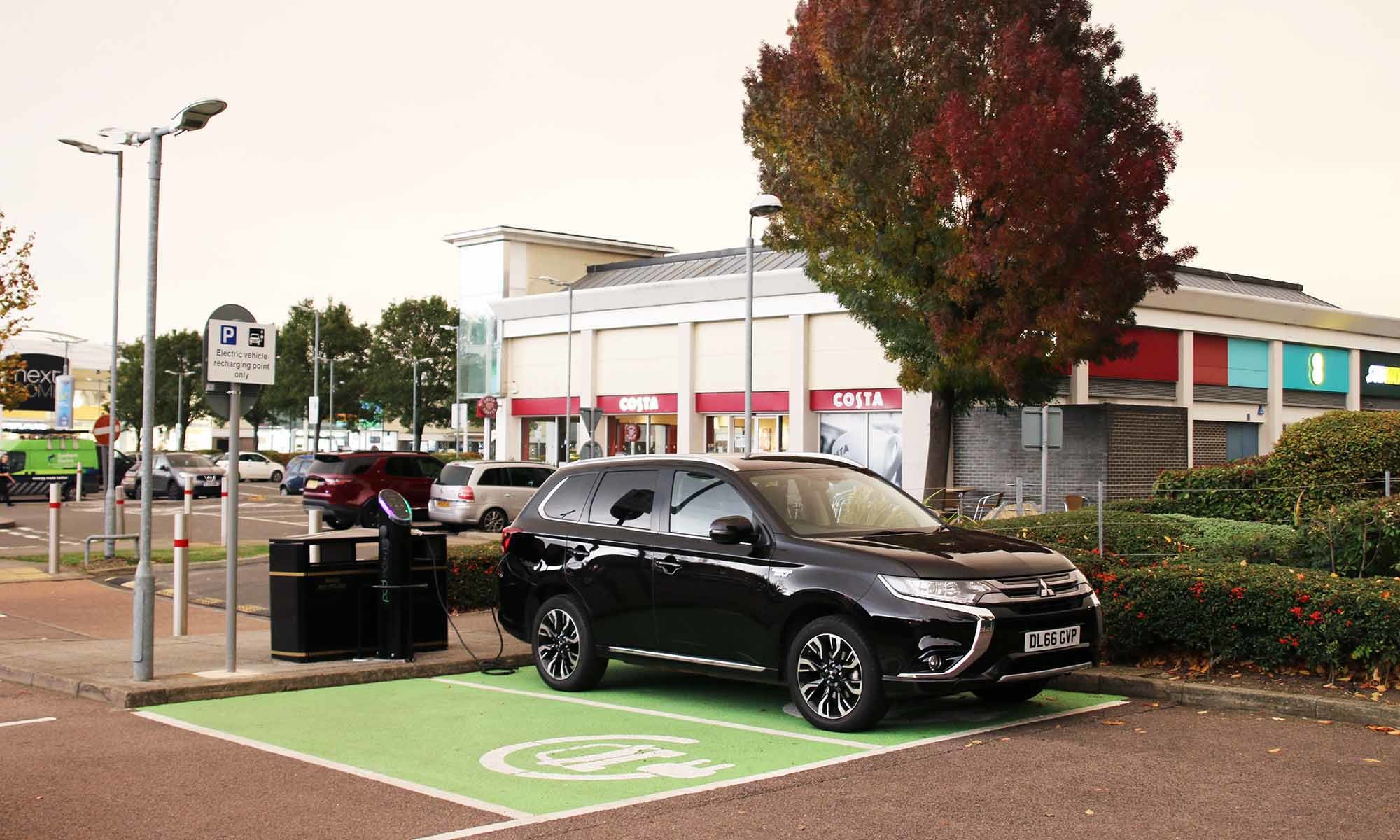 A black SUV parked in a green EV charging bay at the Savill's car park, and plugged into a Pod Point twin charger