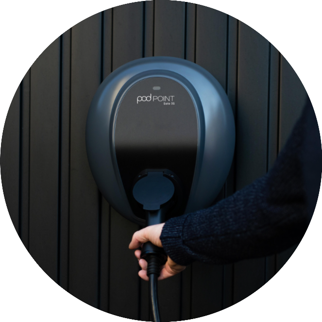 A women's hand is plugging a cable into a Pod Point Solo 3 installed on a wooden slat wall